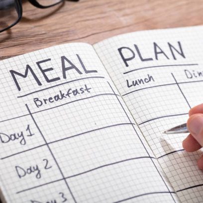 Close-up Of A Human Hand Filling Meal Plan In Checkered Pattern Notebook